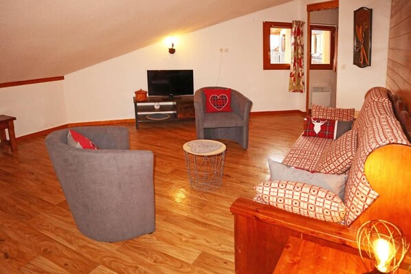 A cozy living room with a sofa, armchairs, a small round table, and a television.