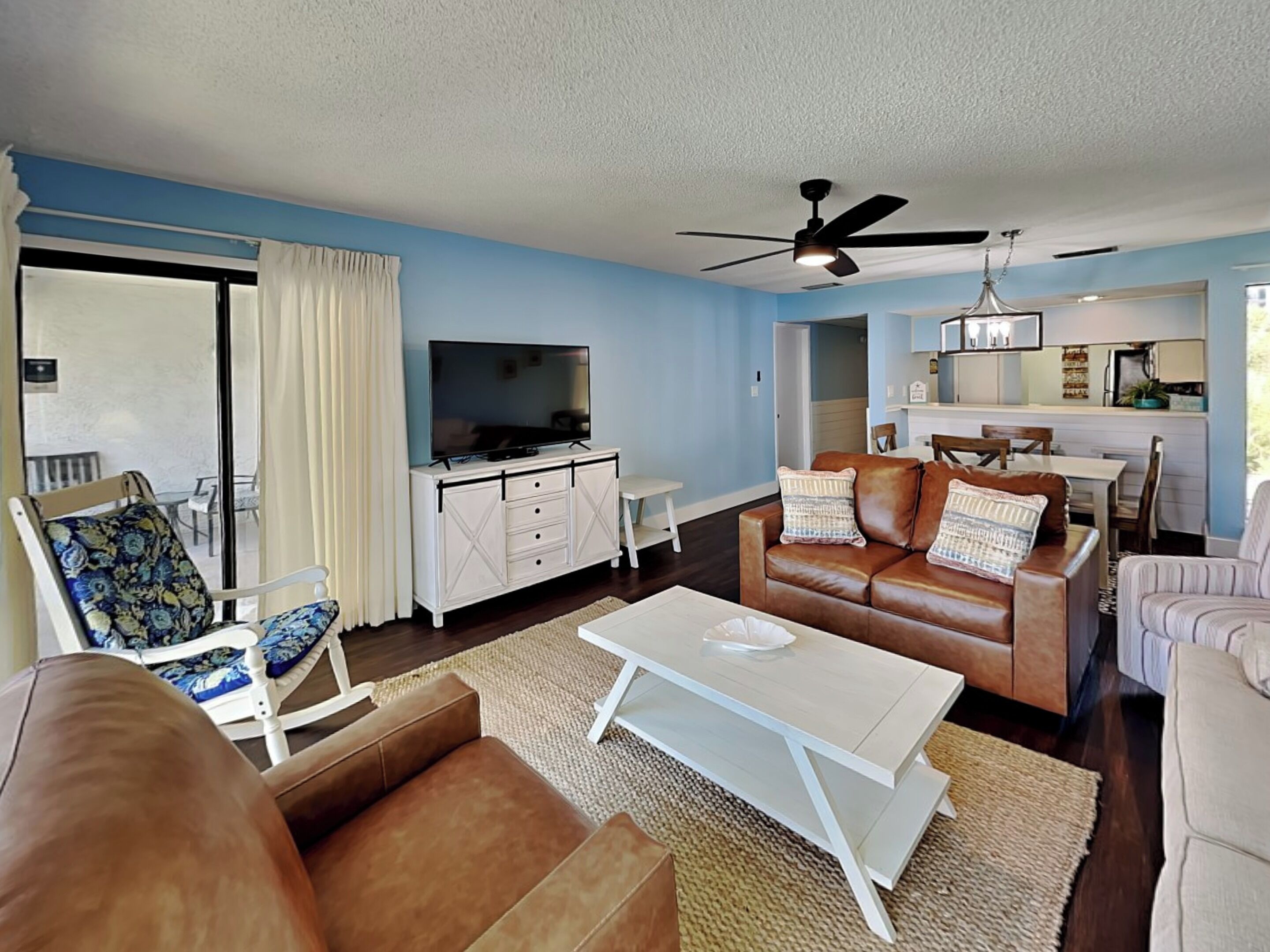 A living room with a TV, leather sofas, a coffee table, and a ceiling fan.
