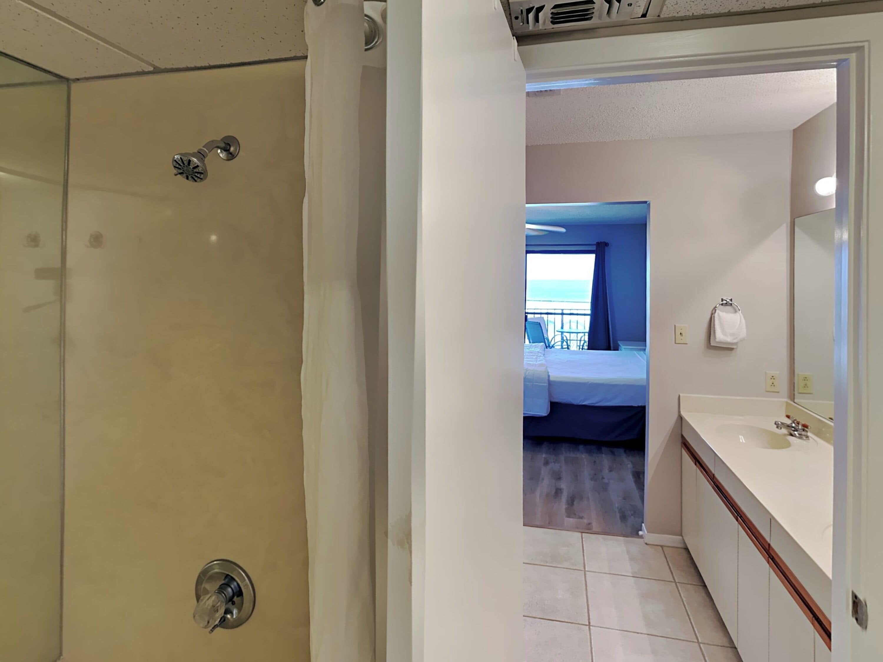 Une chambre d’hôtel avec douche, un lit, une salle de bain avec lavabo et vue sur la mer.