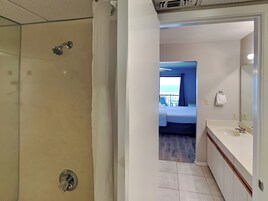 A hotel room with a shower, a bed, a bathroom with a sink, and a view of the sea.