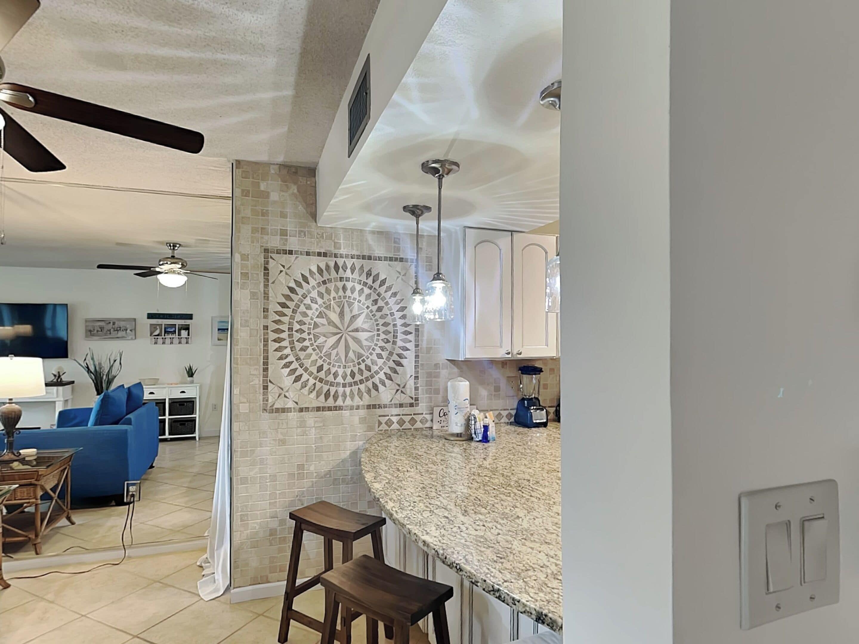 A modern kitchen with a granite countertop, a backsplash with a geometric pattern, and a ceiling fan.