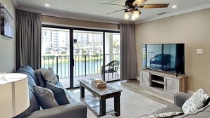 Un salon comprenant un canapé, une table basse, un téléviseur et un balcon offrant une vue sur les immeubles et la verdure.