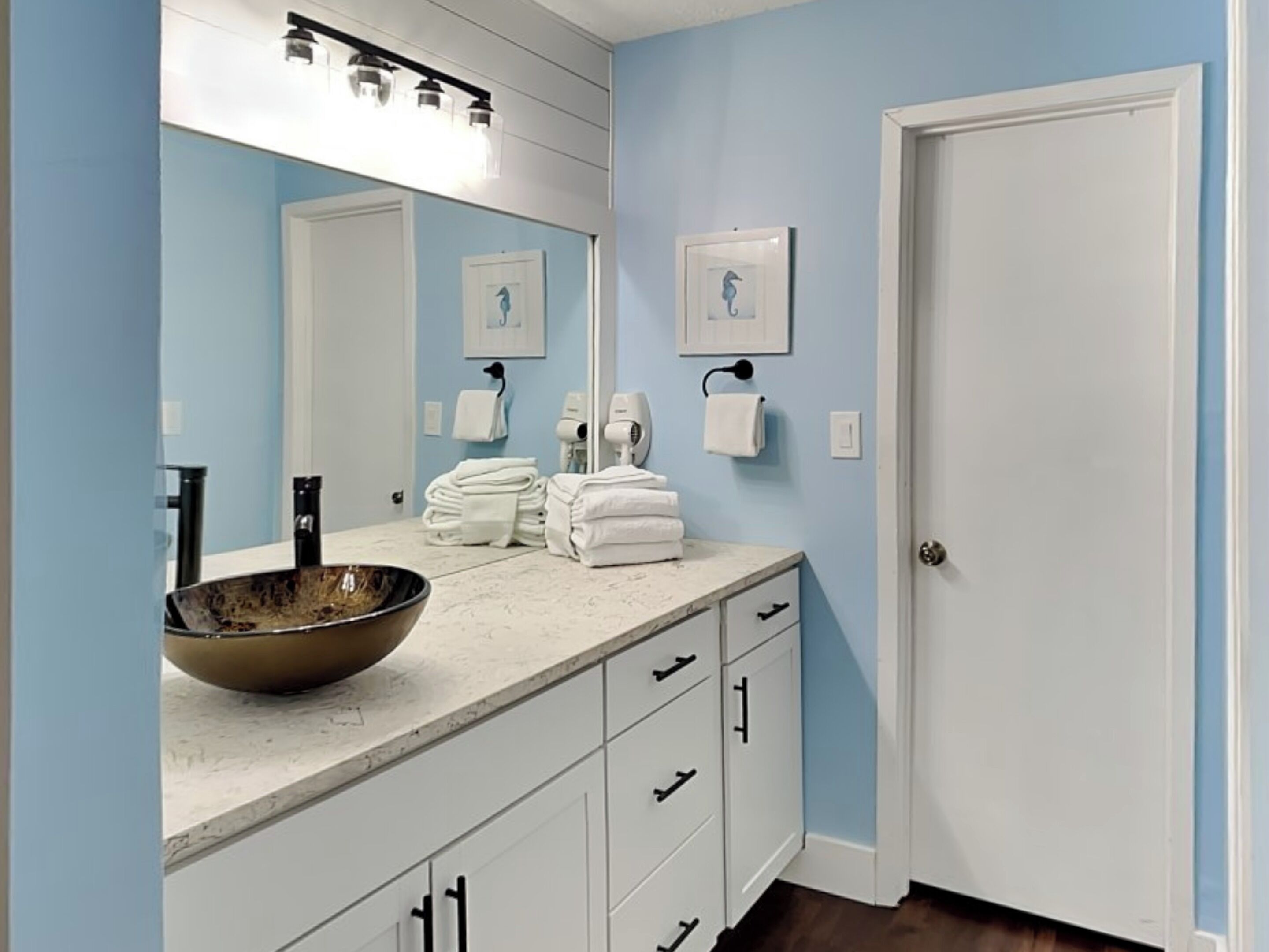 A bathroom with a large mirror, a sink with a bowl, towels stacked on the counter, and a door.