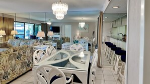 Un salon moderne avec un coin repas, comprenant une table à plateau en verre, des chaises blanches et un lustre.