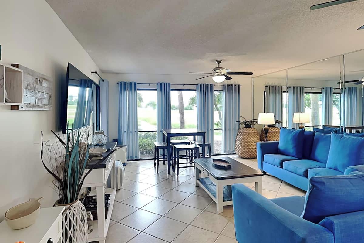 A spacious living room with a blue sofa, a dining table, and a ceiling fan.