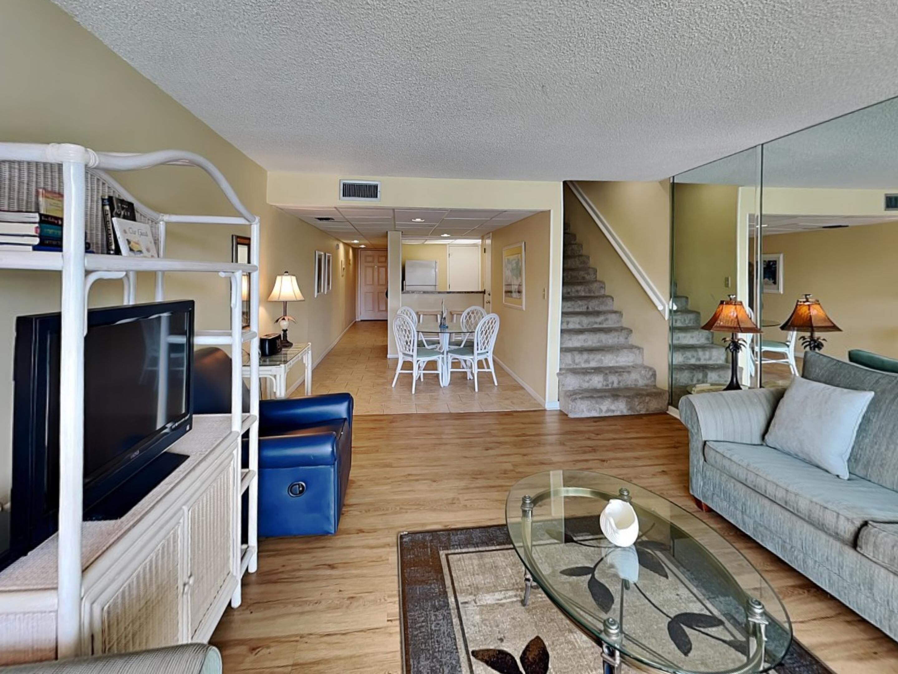 A living room with a TV, sofa, glass coffee table, and a staircase leading to another room.