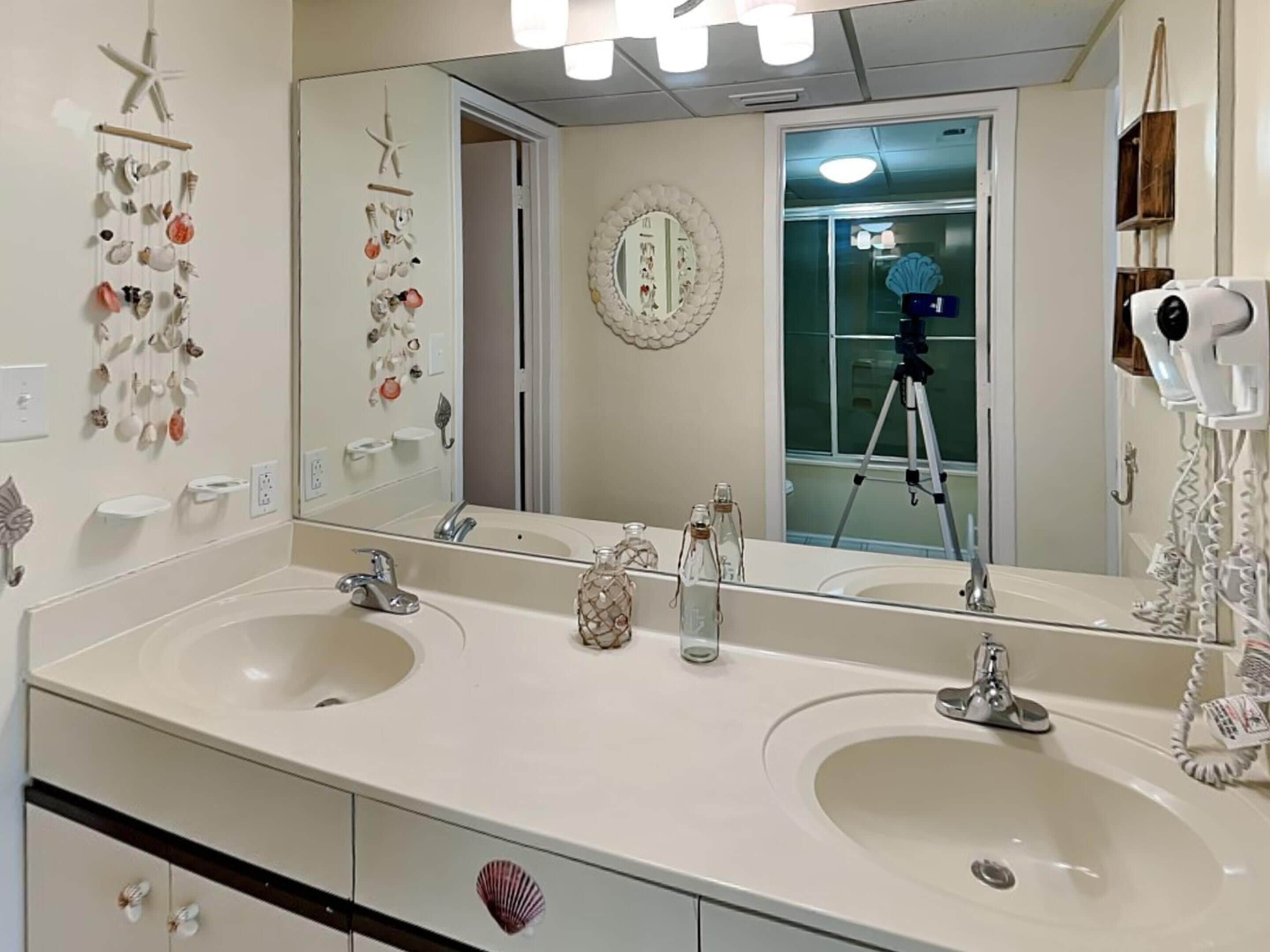 Un baño con dos lavamanos, un espejo grande y conchas decorativas en la pared.