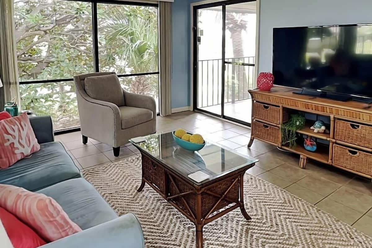 A living room with a sofa, armchair, glass coffee table, and a TV on a wooden cabinet.