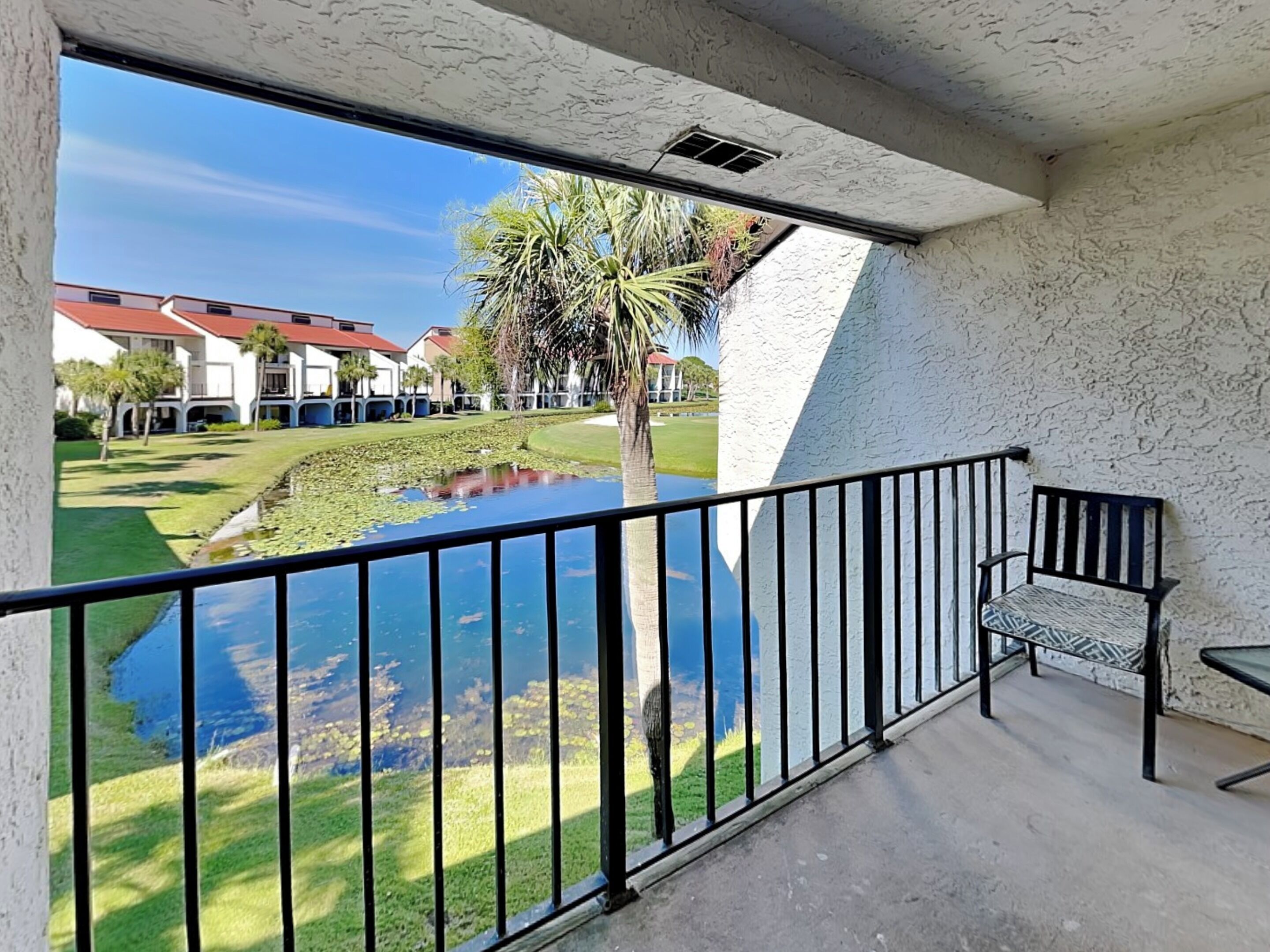 A balcony with a view of a pond, a bench, and a building in the background.