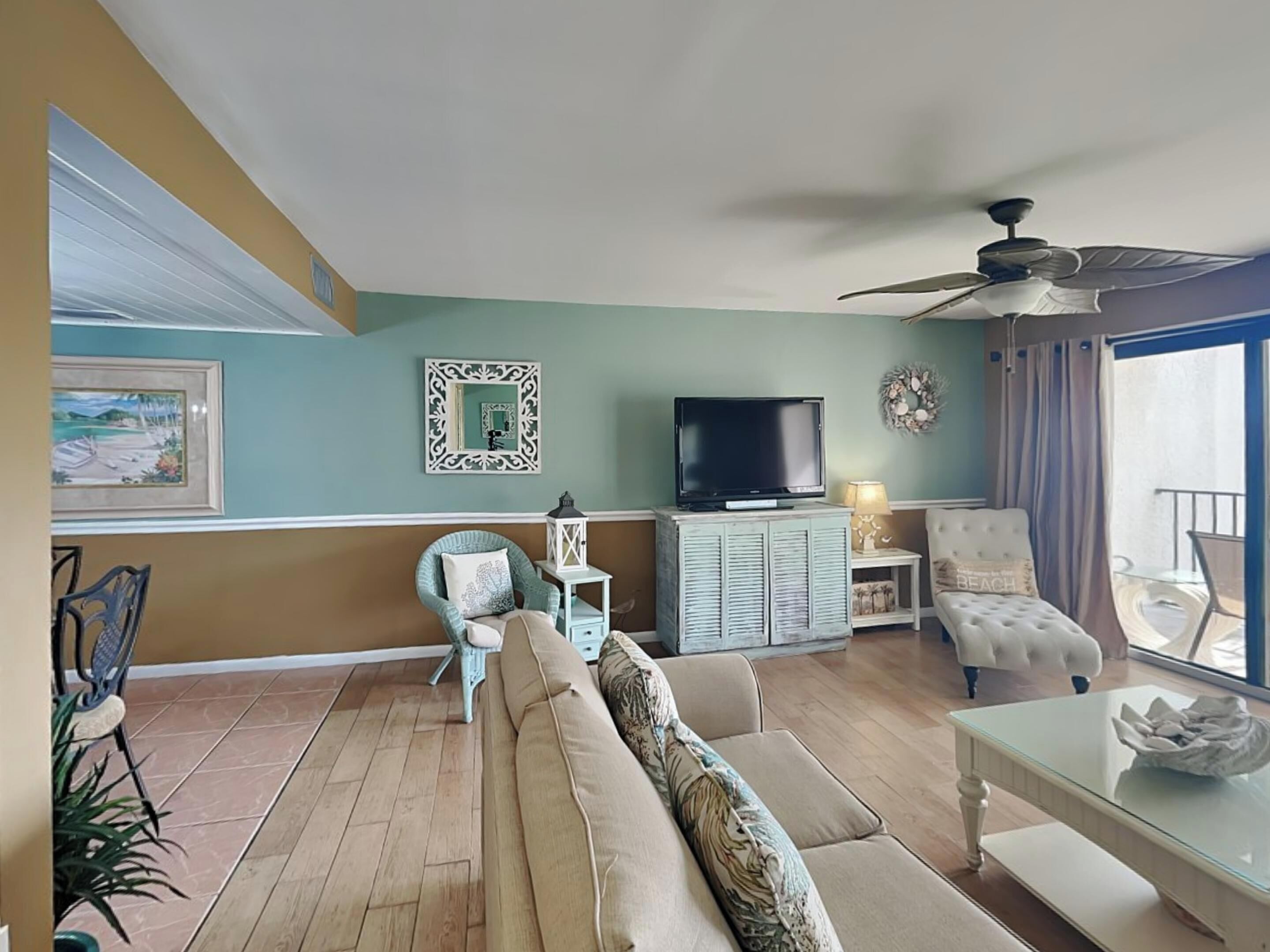 Un salon avec un canapé, un téléviseur, un ventilateur de plafond et un balcon offrant une vue dégagée.