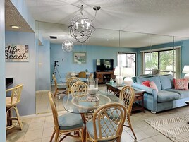 A living room with a glass dining table, wicker chairs, a blue sofa, and a television.