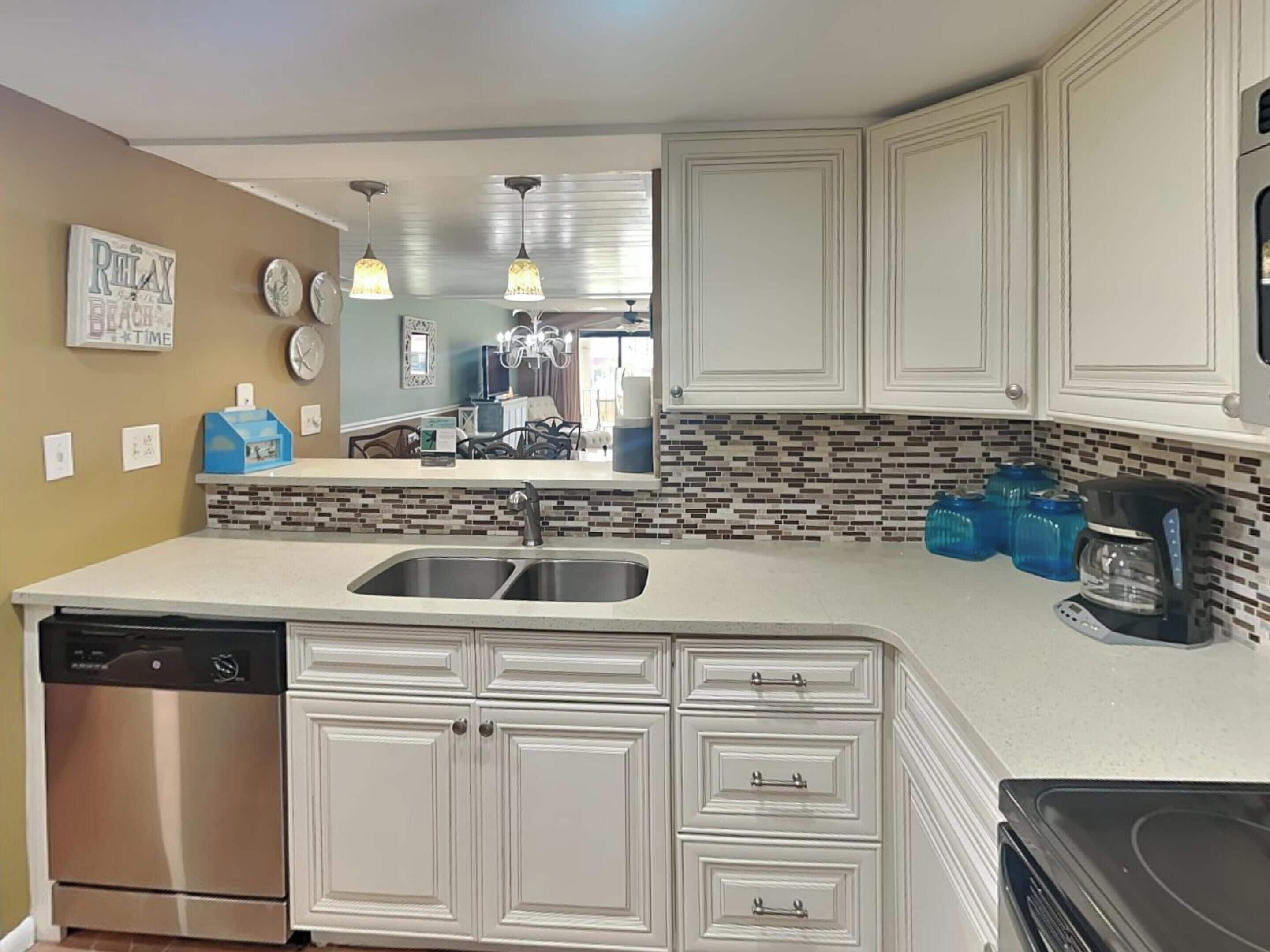 A kitchen with white cabinets, a stainless steel dishwasher, a double sink, and a tiled backsplash.
