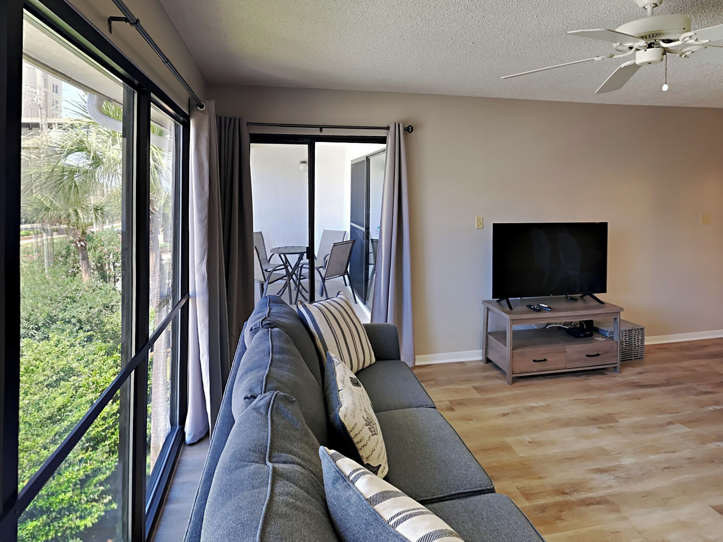 A modern living room with a large sofa, a flat-screen TV, and a balcony with outdoor furniture.