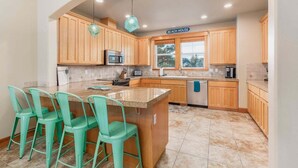A kitchen with wooden cabinets, a granite countertop island with bar stools, and a sign reading "BEACH HOUSE". - Sacred Waters Retreat -updated townhome, near beach. Dog OK. (Pacific City)