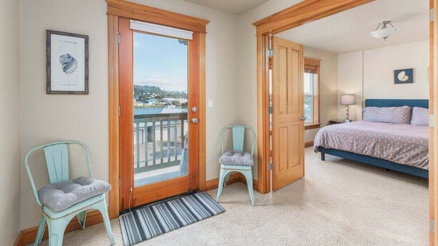 A bedroom with a bed, a door leading to a balcony, and two chairs. - Sacred Waters Retreat -updated townhome, near beach. Dog OK. (Pacific City)