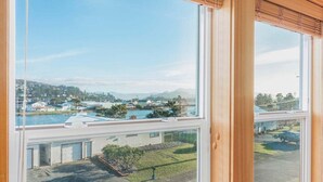 A view from a window overlooking a residential area with a clear sky, a body of water, and a distant hill. - Sacred Waters Retreat -updated townhome, near beach. Dog OK. (Pacific City)