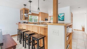 Eine moderne Küche mit Holzausstattung, einer zentralen Kochinsel mit Barhocker, Pendelleuchten und Blick ins Freie.