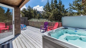 Eine Holzterrasse mit Whirlpool, bunten Adirondack-Stühlen und Blick auf Bäume.