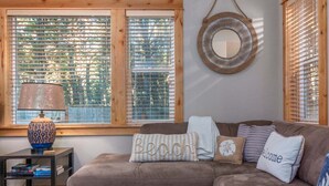 A cozy living room with a brown sofa, a side table with a lamp, and a window with wooden blinds. - Sea Jay-hot tub, 2 blocks to beach, borders forest (Pacific City)