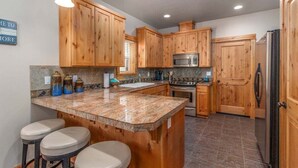 A kitchen with wooden cabinets, granite countertops, a central island with stools, a microwave, stove, and refrigerator. - Sea Jay-hot tub, 2 blocks to beach, borders forest (Pacific City)