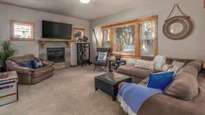 A living room with a fireplace, leather sofas, a flat-screen TV, and a large window with blinds. - Sea Jay-hot tub, 2 blocks to beach, borders forest (Pacific City)