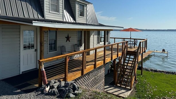 Une maison dotée d’une terrasse donnant sur un plan d’eau, avec un escalier, des sièges d’extérieur et une décoration en forme d’étoile.