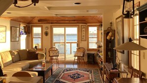Un salon chaleureux avec un plafond en bois, une grande moquette et une vue sur l’eau par les fenêtres.