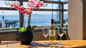 A table with a potted plant, a bottle of wine, and two glasses on a balcony overlooking a cityscape. - 🚢Luxury Seattle Waterfront Walk to Cruise Ship & Pike Place -Waterfront Views🎡 (Seattle)