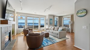 A spacious living room with a fireplace, large windows, and a view of the sea. - 🚢Luxury Seattle Waterfront Walk to Cruise Ship & Pike Place -Waterfront Views🎡 (Seattle)