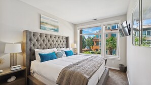 Une chambre avec un grand lit, une vue sur les immeubles et un téléviseur fixé au mur.