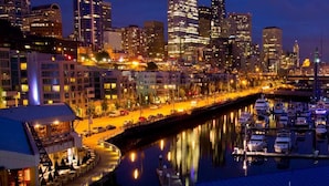 A marina with boats docked, a waterfront promenade, and a city skyline with illuminated buildings and a Ferris wheel. - 🚢Luxury Seattle Waterfront Walk to Cruise Ship & Pike Place -Waterfront Views🎡 (Seattle)