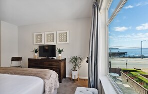 Una camera da letto con un letto, una TV su una cassettiera in legno, una piccola pianta e vista su un molo e sull'acqua.
