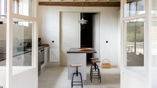 Cocina integrada con una isla central, taburetes y vistas al exterior.