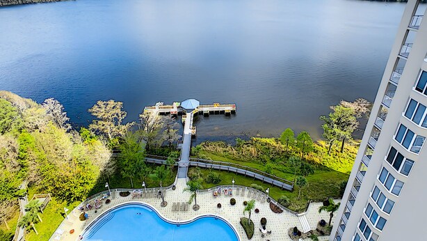 A large swimming pool surrounded by a deck with lounge chairs and a bridge leading to a dock.