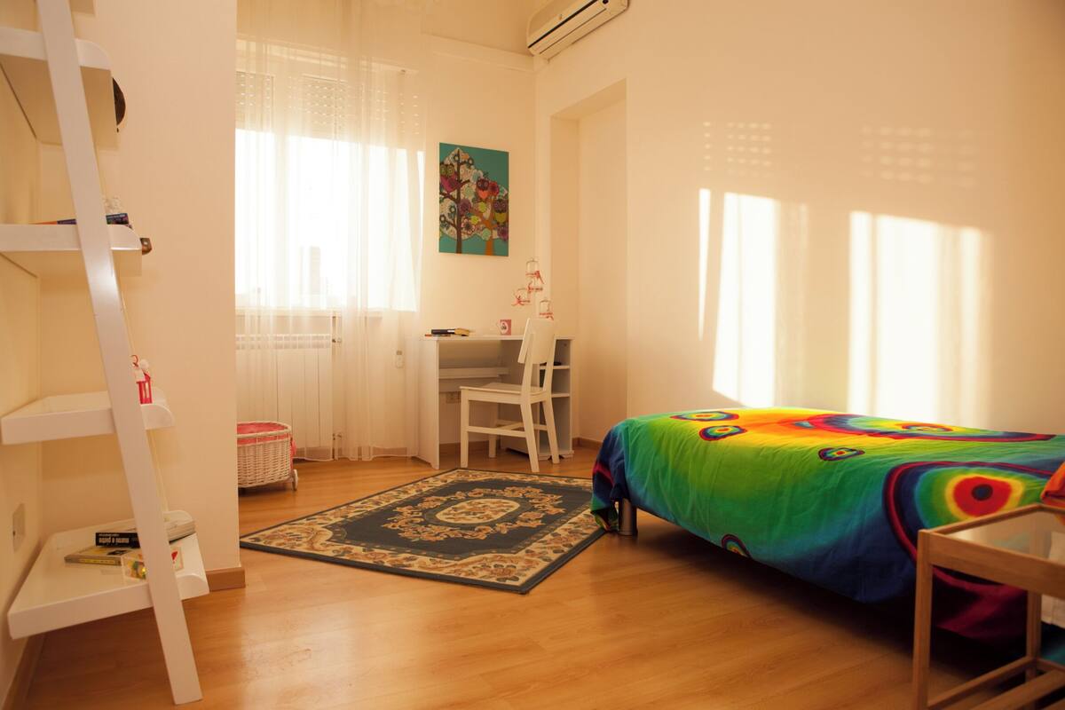 Une chambre à coucher avec un lit, un bureau, une chaise, une échelle et une fenêtre avec des rideaux.