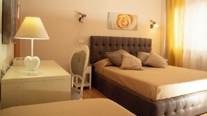 Quarto de hotel com uma cama, uma escrivaninha com abajur, uma cadeira e uma obra de arte na parede.