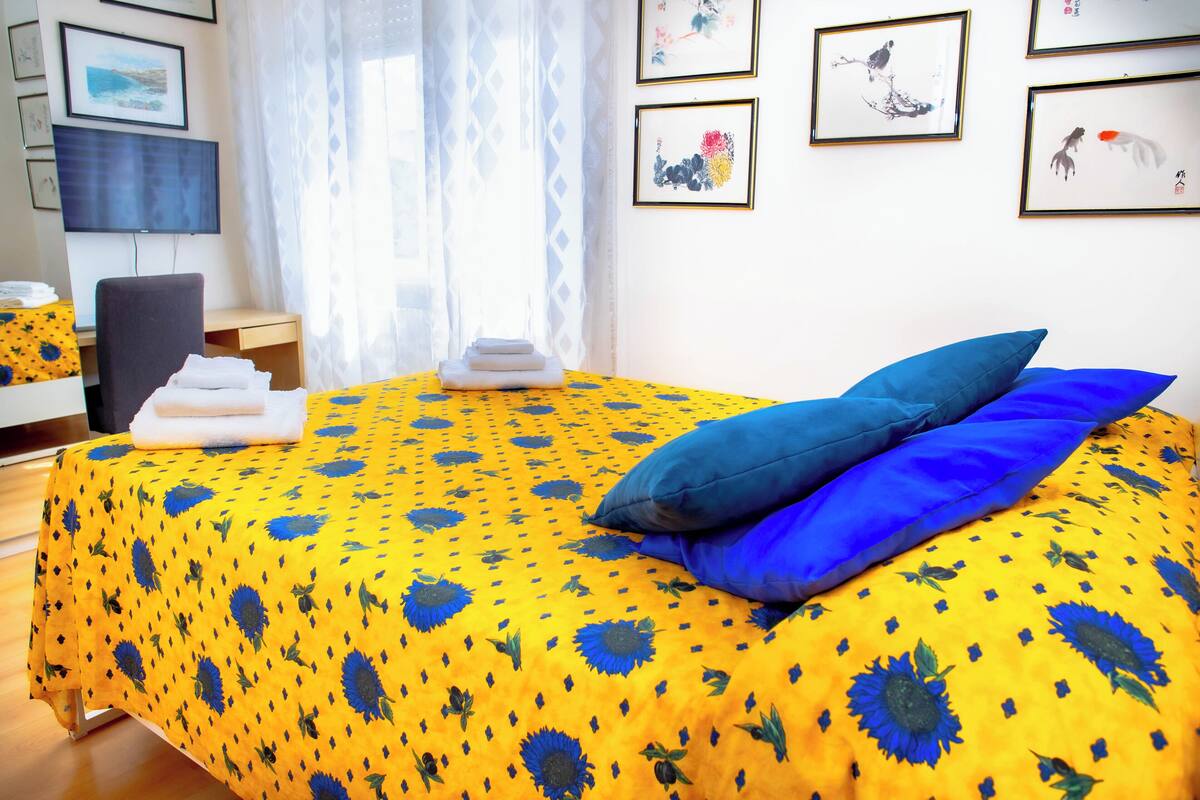 Un lit bien fait, recouvert d’une couvre-lit à motifs floraux jaunes, avec deux oreillers bleus et une pile de serviettes pliées posée sur le côté.