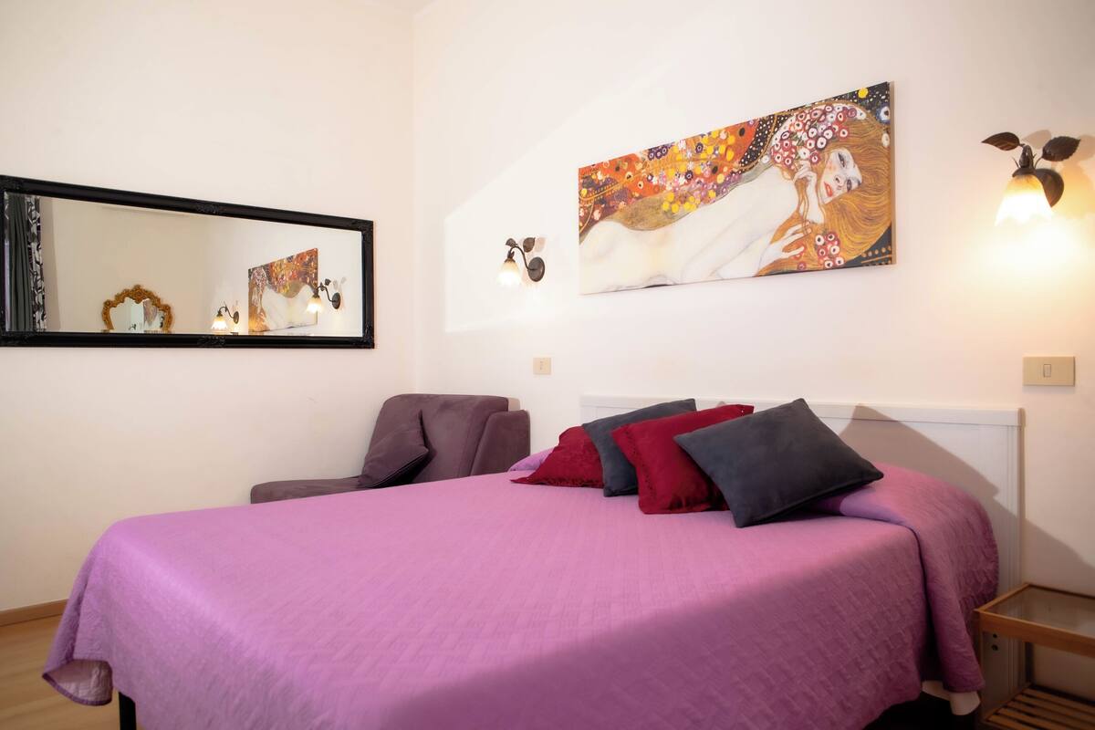 Une chambre à coucher avec un grand lit, une chaise, un miroir fixé au mur et un tableau.