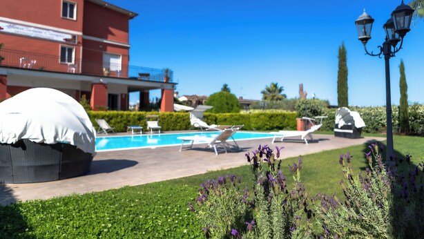 Área da piscina com espreguiçadeiras, um espaço coberto para relaxar e um edifício com fachada vermelha.