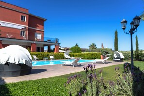 Zona de piscina amb gandules, un espai d'estar cobert i un edifici amb façana vermella.
