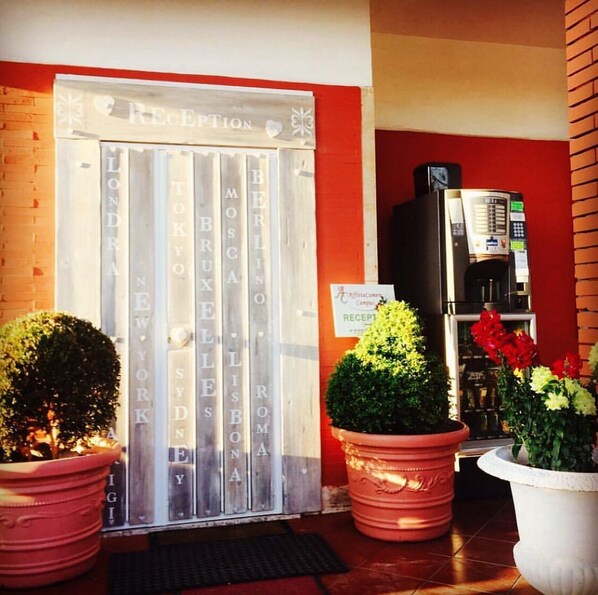 Entrada d'hotel amb una taquilla, un senyal que indica zona de recepció i plantes en testos.