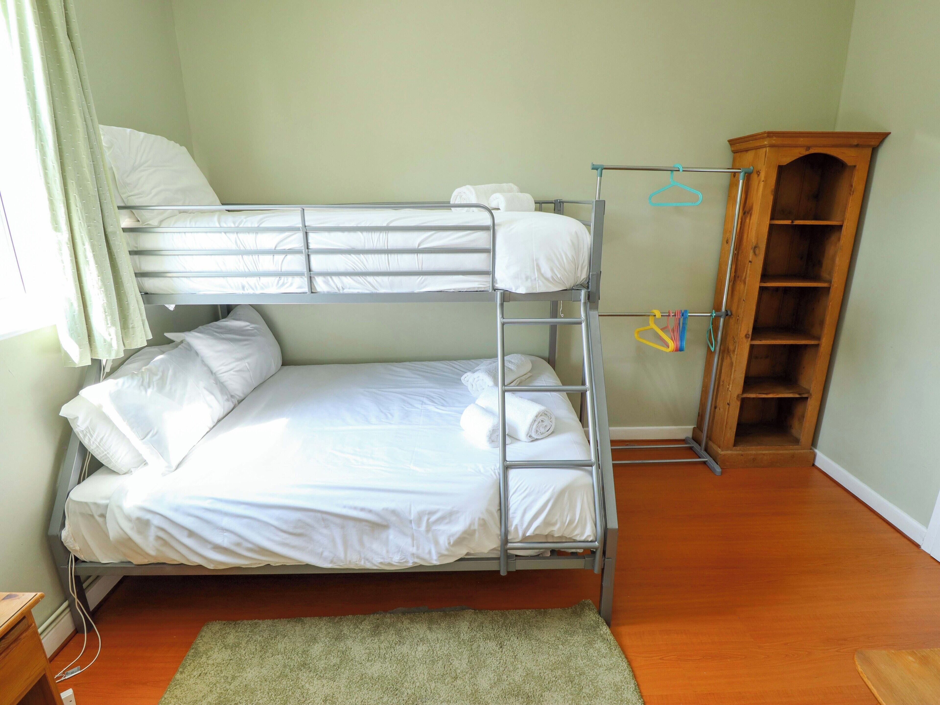 Ein Stockbett mit weißer Bettwäsche, ein Holzschrank und ein grüner Teppich auf Holzboden.