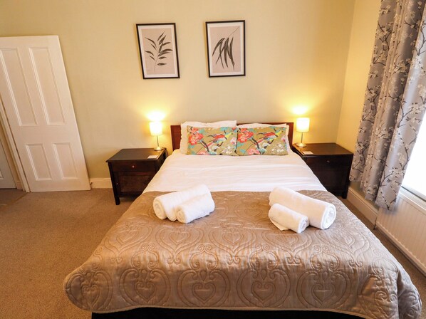 A hotel room with a large bed, two bedside lamps, floral pillows, and a decorative headboard.