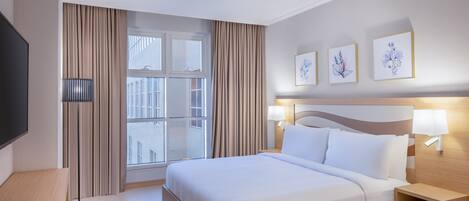 A hotel room with a large bed, bedside lamps, a TV, and a window with curtains.