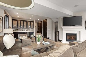 A modern living room with a sofa, coffee table, and fireplace. There is a kitchen in the background with cabinets and a dining area.