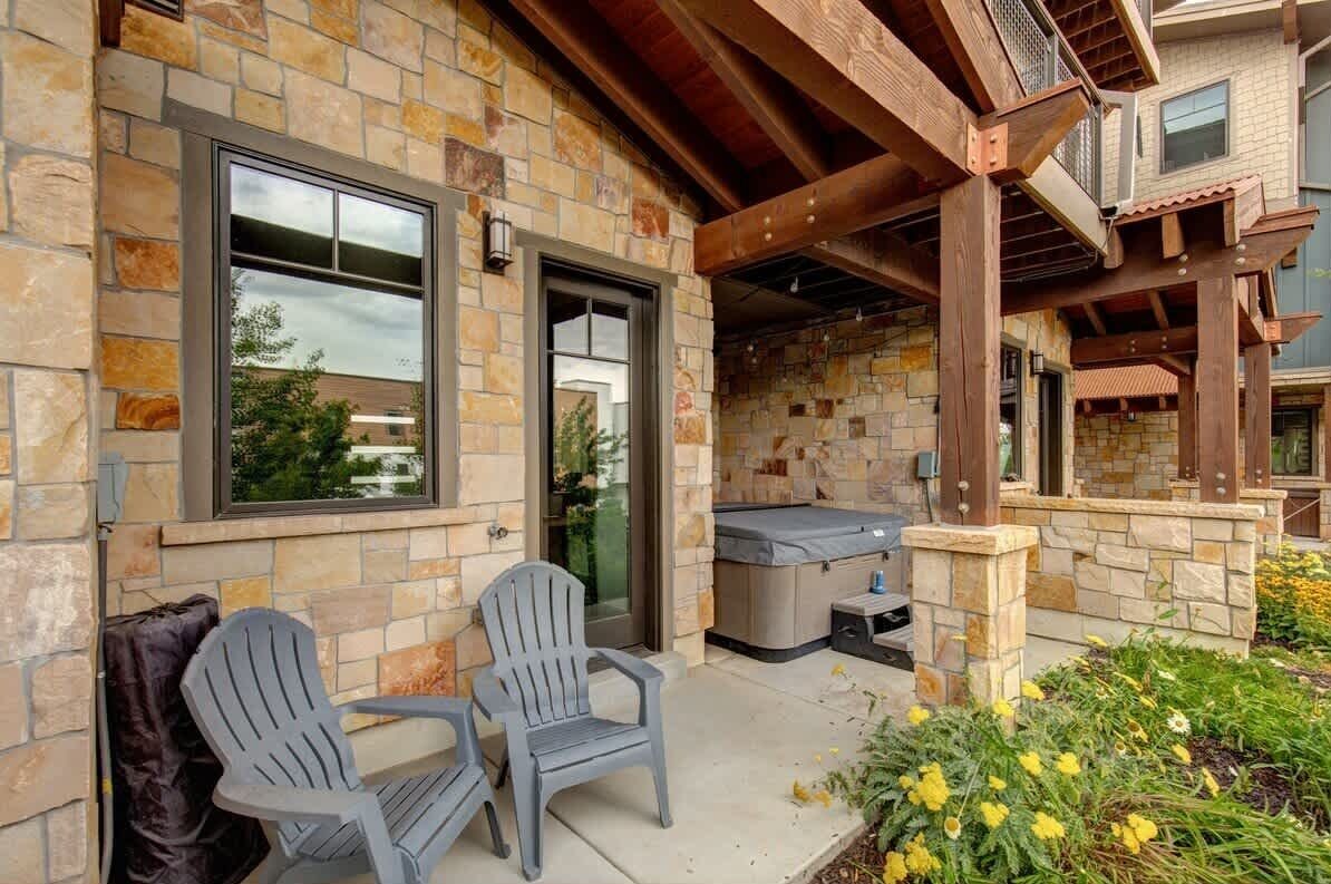 Un edificio de piedra con dos sillas Adirondack, un porche cubierto y un jacuzzi.