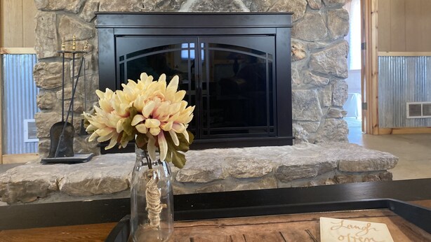 A stone fireplace with a glass door, a vase with flowers, and a sign reading "Length of Time". - Charming Secluded Getaway Cabin within minutes of amenities  (Cape girardeau)