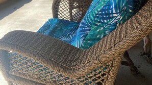 A wicker chair with a blue patterned cushion, a small table with a vase of yellow flowers, and a stone wall in a covered outdoor area. - Charming Secluded Getaway Cabin within minutes of amenities  (Cape girardeau)