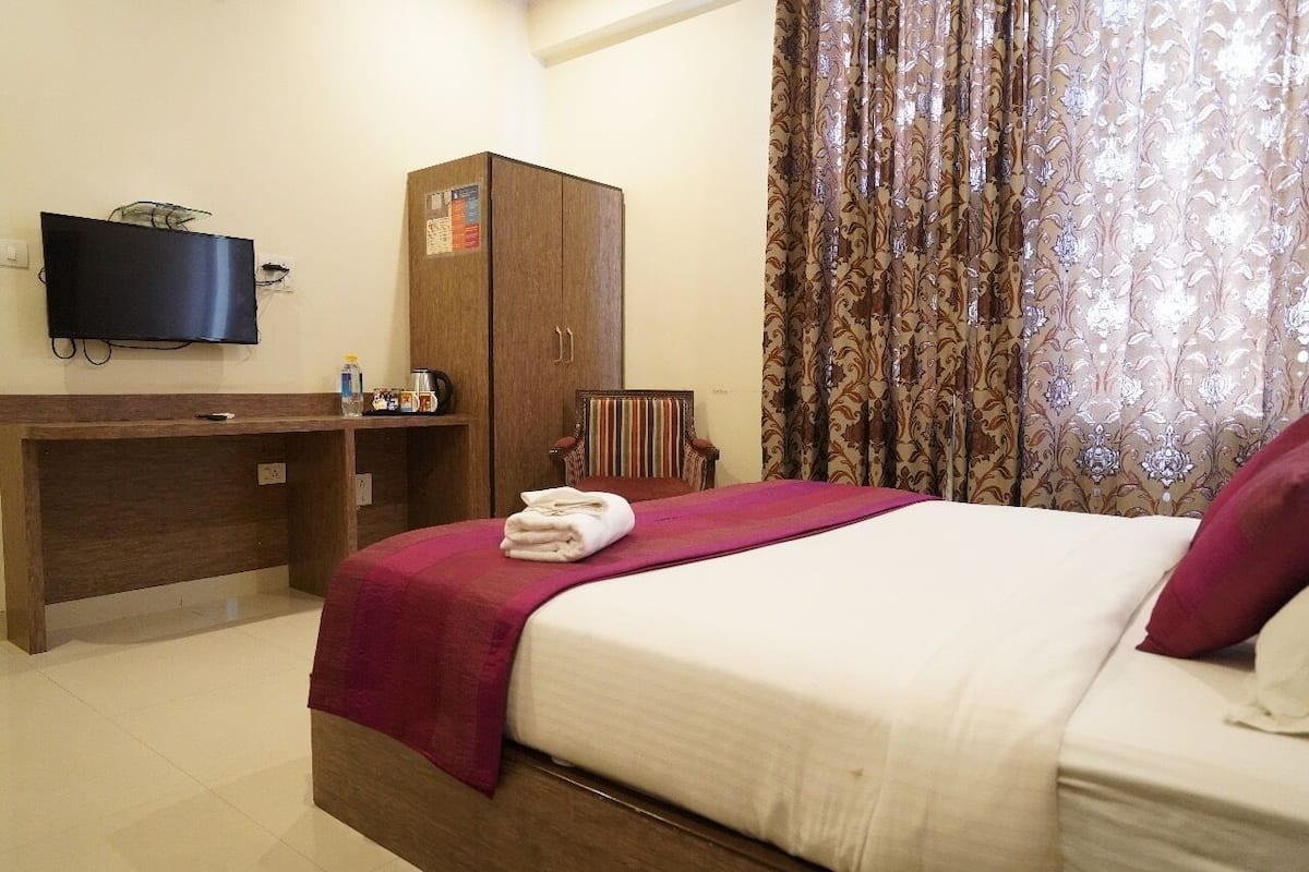 A hotel room with a bed, a wooden desk, a television, and a patterned curtain.