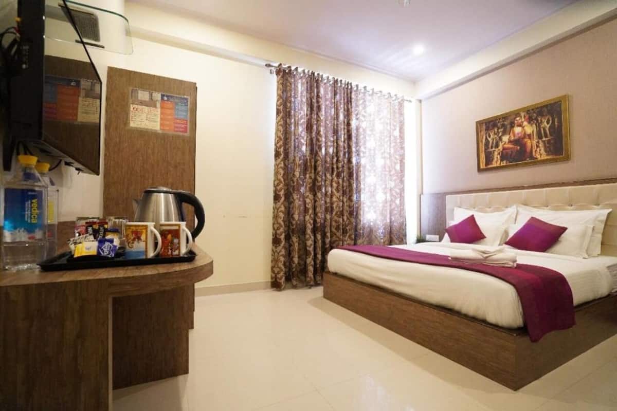 A hotel room with a bed, a desk with a kettle, a water bottle, and a tray with snacks.